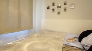 Un dormitori petit i ben organitzat, amb un llit individual, una finestra amb cortina i una paret decorada amb diverses fotografies petites.