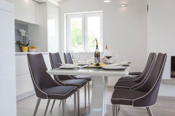 A modern dining area with a white table set for four, surrounded by dark upholstered chairs. - Luxury villa Retro fusion in Tucepi (Tucepi)