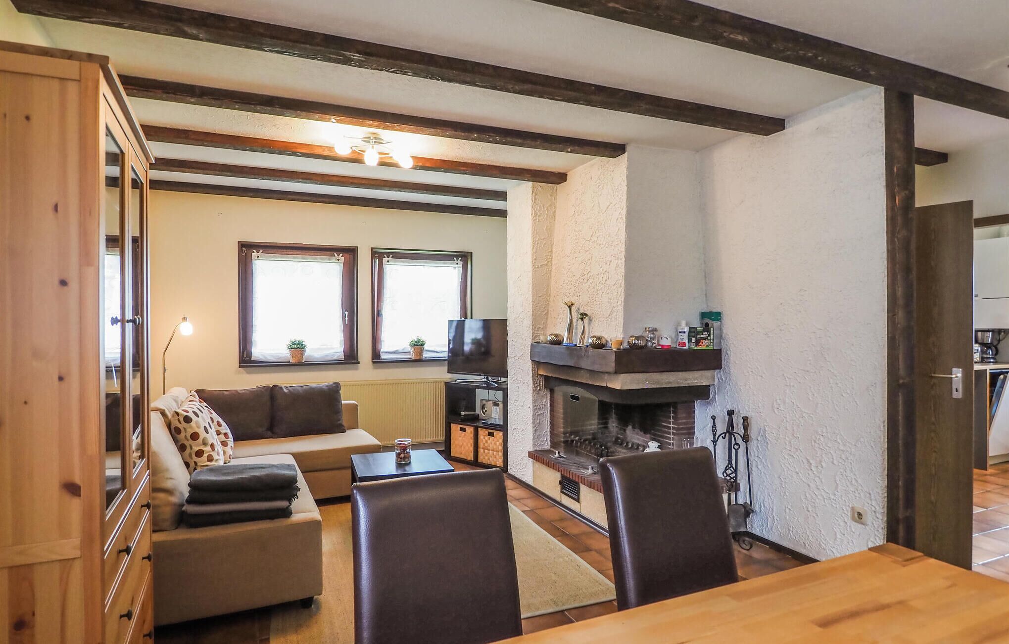 A cozy living room with a sofa, a TV, and a fireplace. There are windows with curtains and a wooden ceiling.