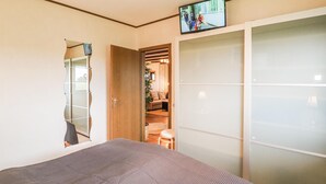 Ein Schlafzimmer mit einem Bett, einem an der Wand befestigten Fernseher und einem Schiebetürenschrank.