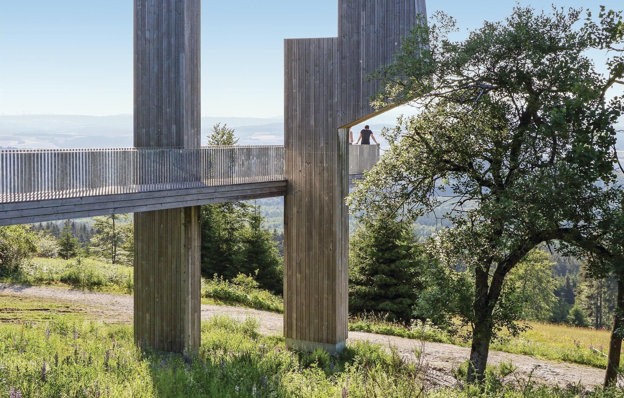 Een houten brug met een metalen leuning, ondersteund door verticale houten balken, die twee verhoogde platforms verbindt.