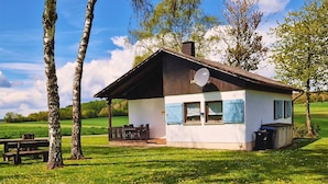 Ein kleines, eingeschossiges Haus mit geneigtem Dach, einer Satellitenschüssel und einem eingezäunten Patio mit Tisch und Stühlen.