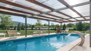 Une piscine extérieure couverte, dotée de chaises longues et d’une structure en forme de pergola.