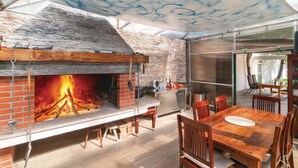 Un espace de restauration extérieur moderne, doté d’une cheminée en briques, de mobilier en bois et d’une structure vitrée.
