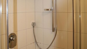 Ducha con puerta de vidrio, grifería cromada y paredes con azulejos.
