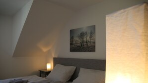 Un dormitorio con cama, almohadas, una mesita de noche, un cuadro en la pared y una lámpara.