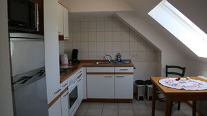 Una cocina compacta con microondas, horno, lavabo y una pequeña mesa de comedor con un mantel individual.
