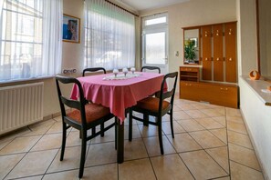 A dining area with a pink tablecloth, four chairs, a wooden cabinet, and a radiator. - Vacation apartment Kruggel 2 (Zinnowitz)