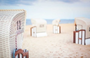 Wicker beach chairs with white cushions on a sandy beach. - Vacation apartment Kruggel 2 (Zinnowitz)