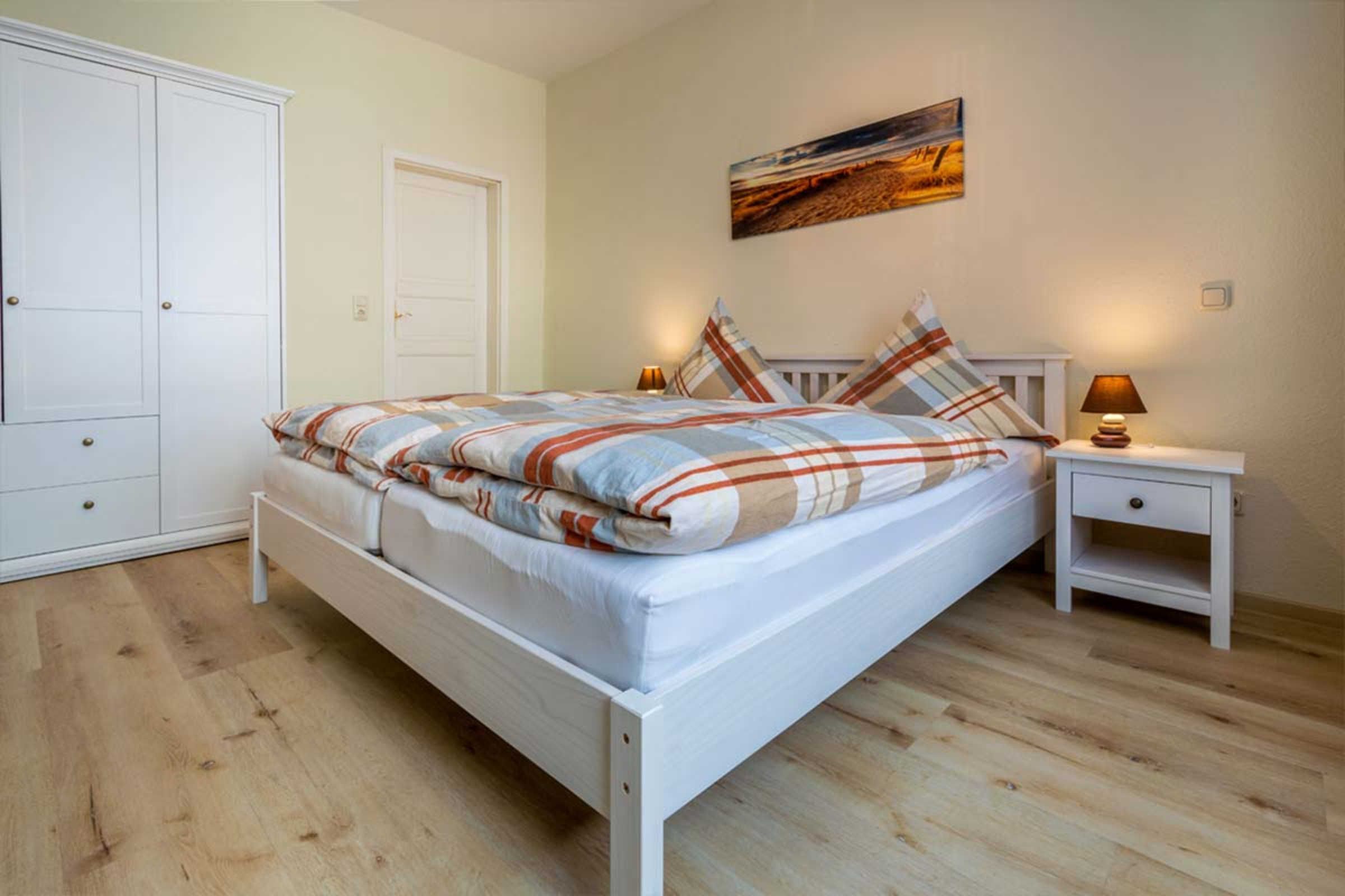 A bedroom with a bed, a nightstand, a wardrobe, and a painting on the wall.