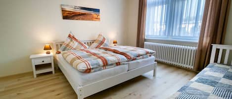 Un dormitorio con cama, mesita de noche, lámpara, radiador y ventana con cortinas.