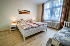 A bedroom with a bed, a nightstand, a lamp, a radiator, and a window with curtains. - Vacation apartment Kruggel 2 (Zinnowitz)