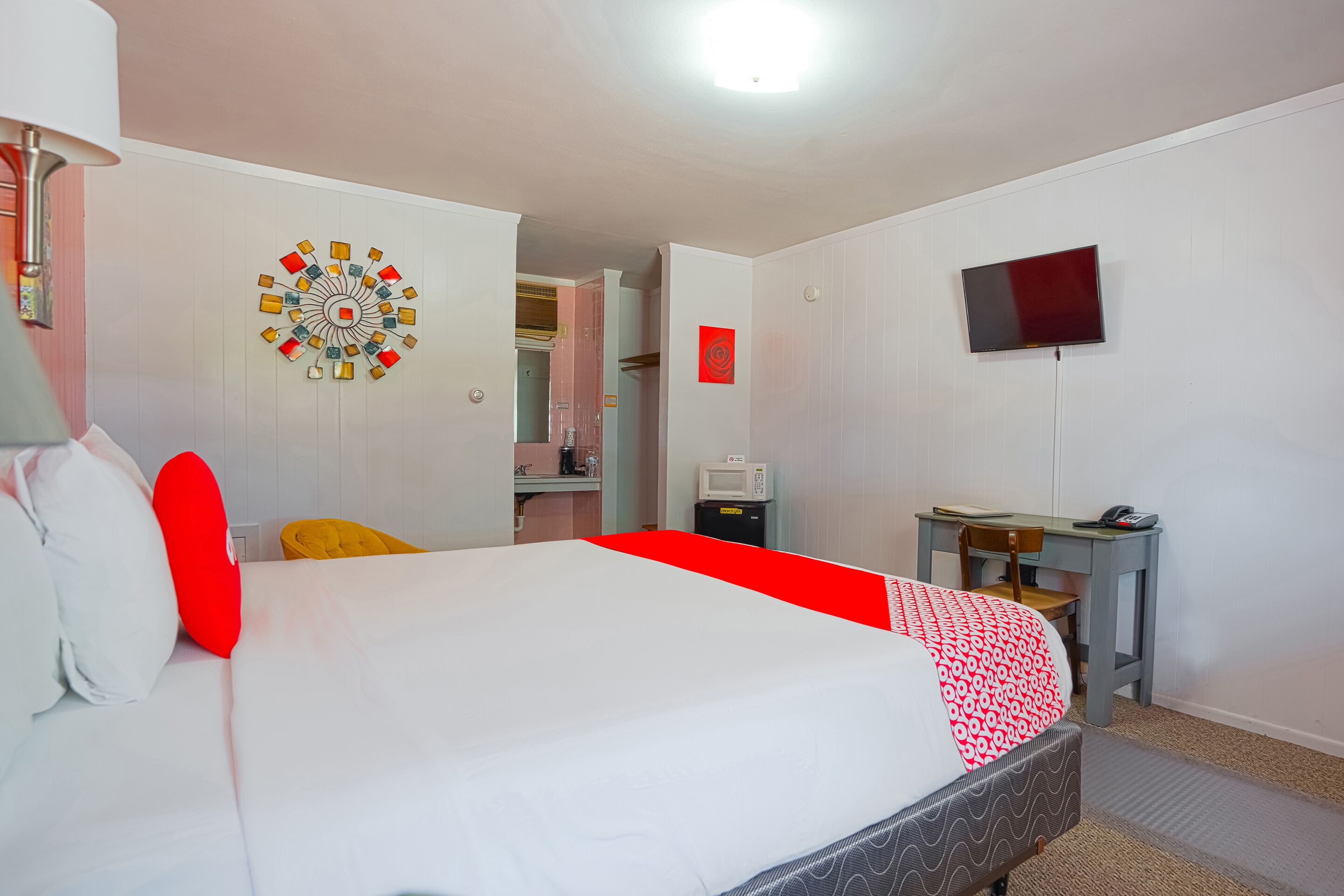 Quarto de hotel com cama, escrivaninha, televisão e micro-ondas.