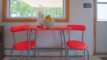 Una mesa roja con dos sillas a juego, un bol con plátanos y un dispensador de toallas de papel.
