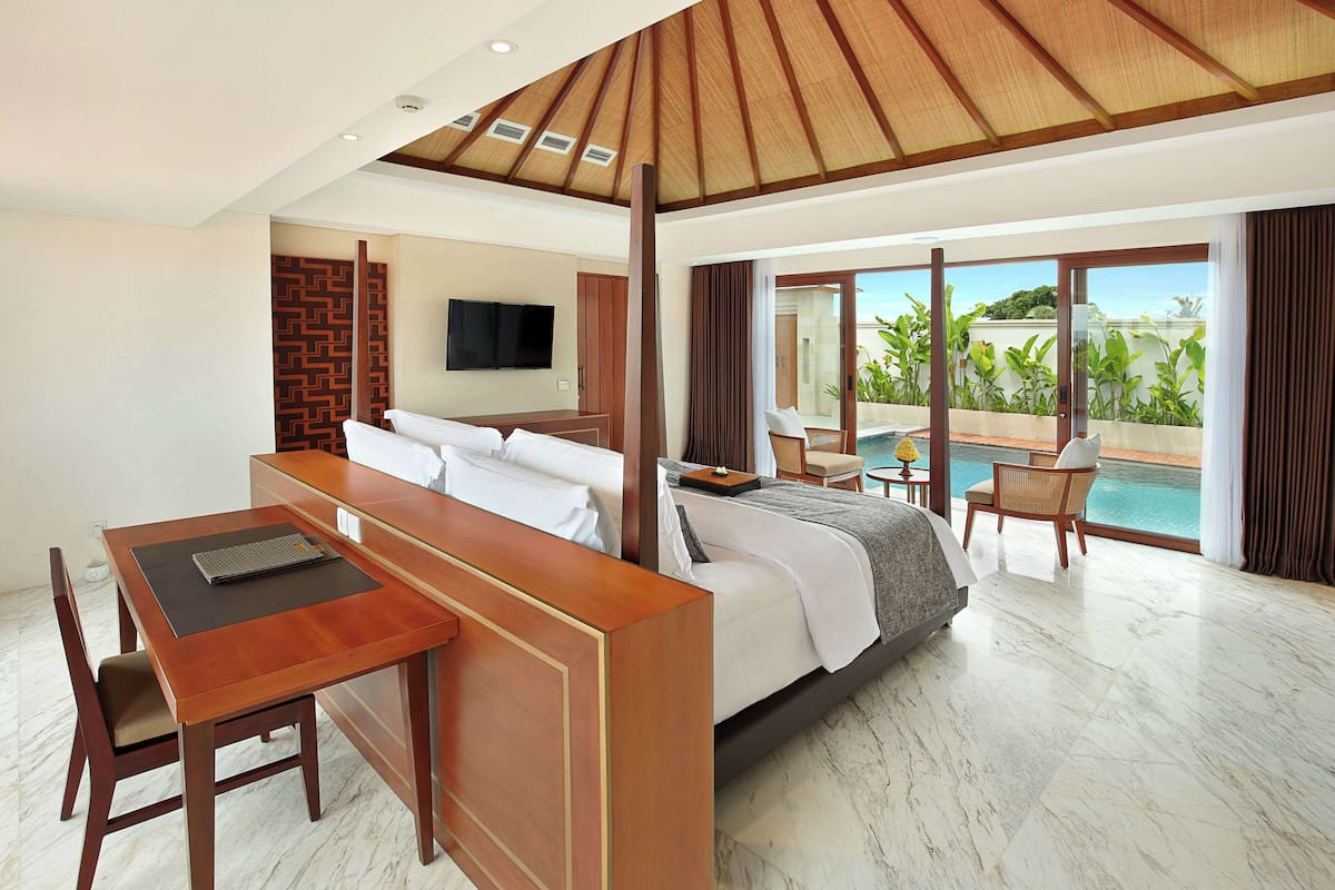 A hotel room with a bed, a desk, a chair, a television, and a view of a pool.