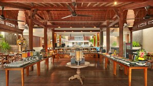A spacious dining area with wooden tables and chairs, a central buffet table, and a ceiling fan. - Royal Suites at The Bandha (Legian)