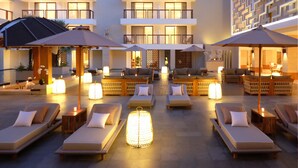 A hotel lobby with multiple lounge areas, each with a cushioned chair and a table, and a central area with a decorative light fixture. - Royal Suites at The Bandha (Legian)