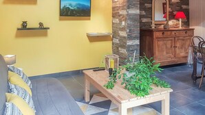 Een woonkamer met een bank, een houten tafel met planten, een televisie aan de muur, een houten kast en een spiegel.