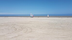 Een breed zandstrand met twee zeilboten en een uitkijktoren.