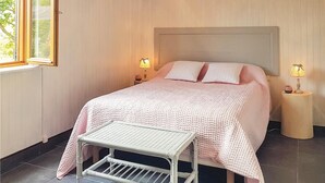 Een netjes opgemaakt bed met hoofdbord, twee bedlampen, een klein tafeltje en een raam met uitzicht op groen.