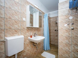 Kylpyhuone, jossa on wc, pesuallas, peili, suihku ja sininen suihkuverho.