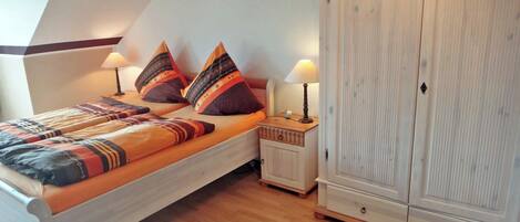 Un dormitorio con una cama, dos mesitas de noche, un armario y una alfombra estampada.