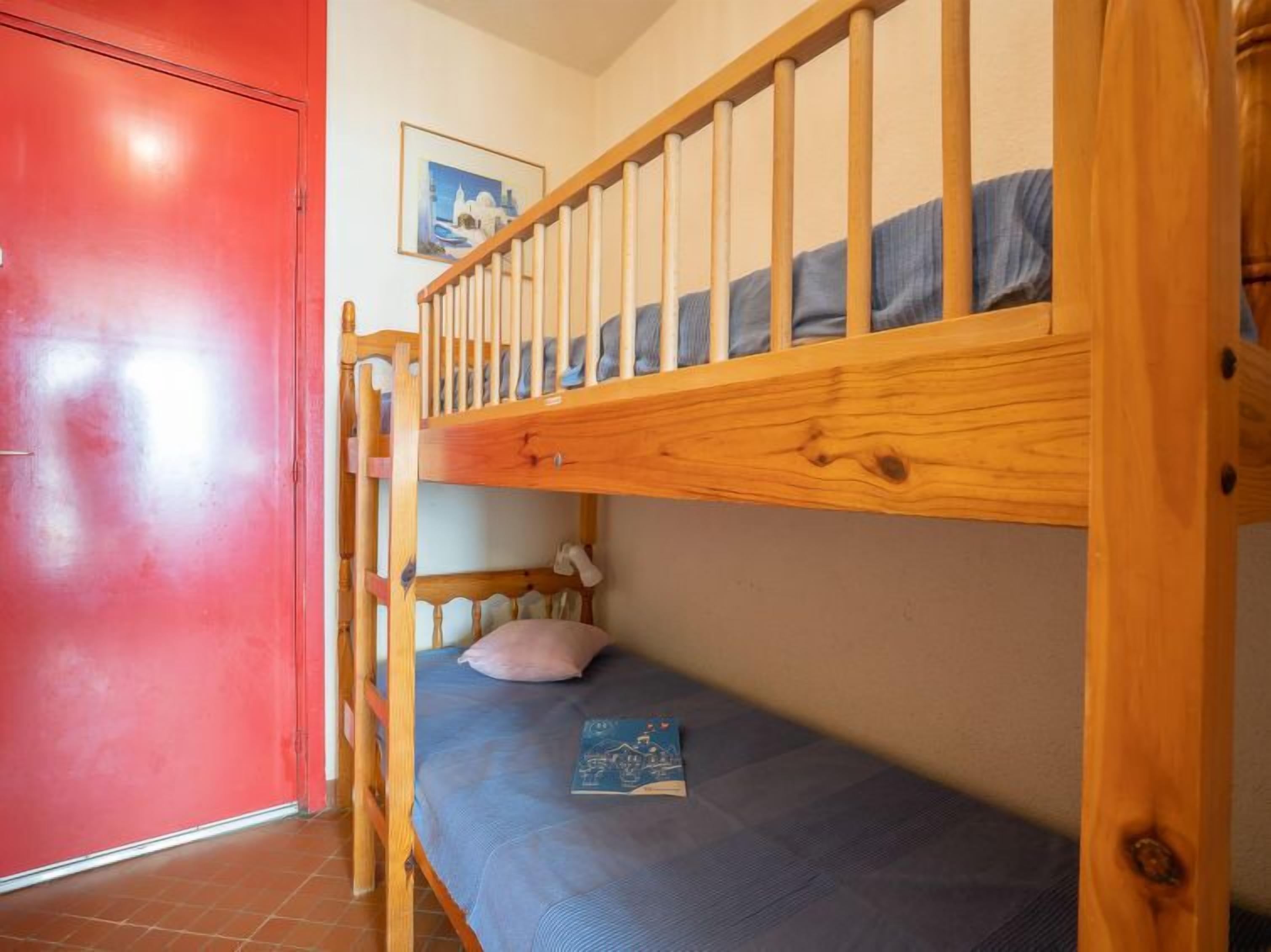 A bunk bed with a blue mattress and a pillow, a red door, and a framed picture on the wall.