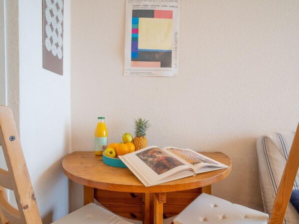 Une table en bois sur laquelle se trouvent un saladier de fruits, une bouteille de jus et un magazine ouvert.