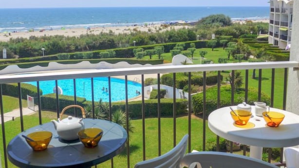 Balcón con vista a una piscina, playa y jardín ajardinado.
