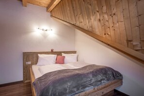 A bedroom with a wooden headboard, a bed with white bedding, a red pillow, and a light fixture on the wall.