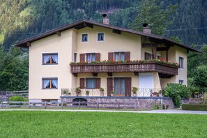 Ein zweistöckiges Gebäude mit Balkon, Steinfundament und Bergelandschaft im Hintergrund.