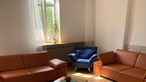 A living room with two orange sofas, a blue armchair, and a small wooden coffee table. - Group accommodation Durbach (Durbach)
