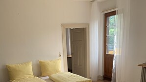 A bedroom with two beds, each with yellow pillows and blankets, wooden flooring, and a door leading to another room. - Group accommodation Durbach (Durbach)