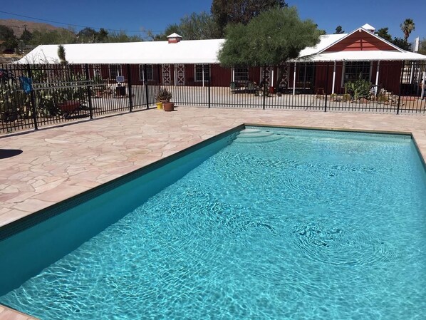 Una piscina rectangular con agua azul cristalina, rodeada por un patio de piedra y una valla de metal negro.