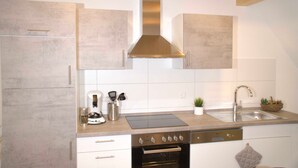 Une cuisine moderne avec des armoires blanches, une hotte de cuisinière en acier inoxydable, un four encastré et un évier.