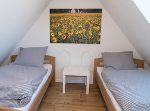 Une chambre avec deux lits simples, une petite table blanche et un tableau représentant des tournesols accroché au mur.