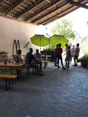 Un espace extérieur aménagé en terrasse, avec un revêtement de sol hexagonal, des tables en bois et des parasols verts offrant de l’ombre.