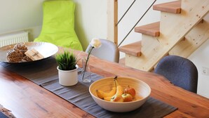 Une table de salle à manger en bois, sur laquelle se trouvent un saladier rempli de fruits, une assiette de biscuits et une petite plante en pot.