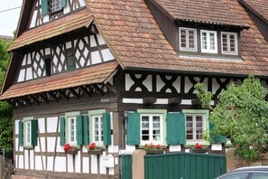 Une maison traditionnelle à colombages, dotée d’un toit à forte pente, de nombreuses fenêtres avec volets et de jardinières sur les rebords de fenêtre.