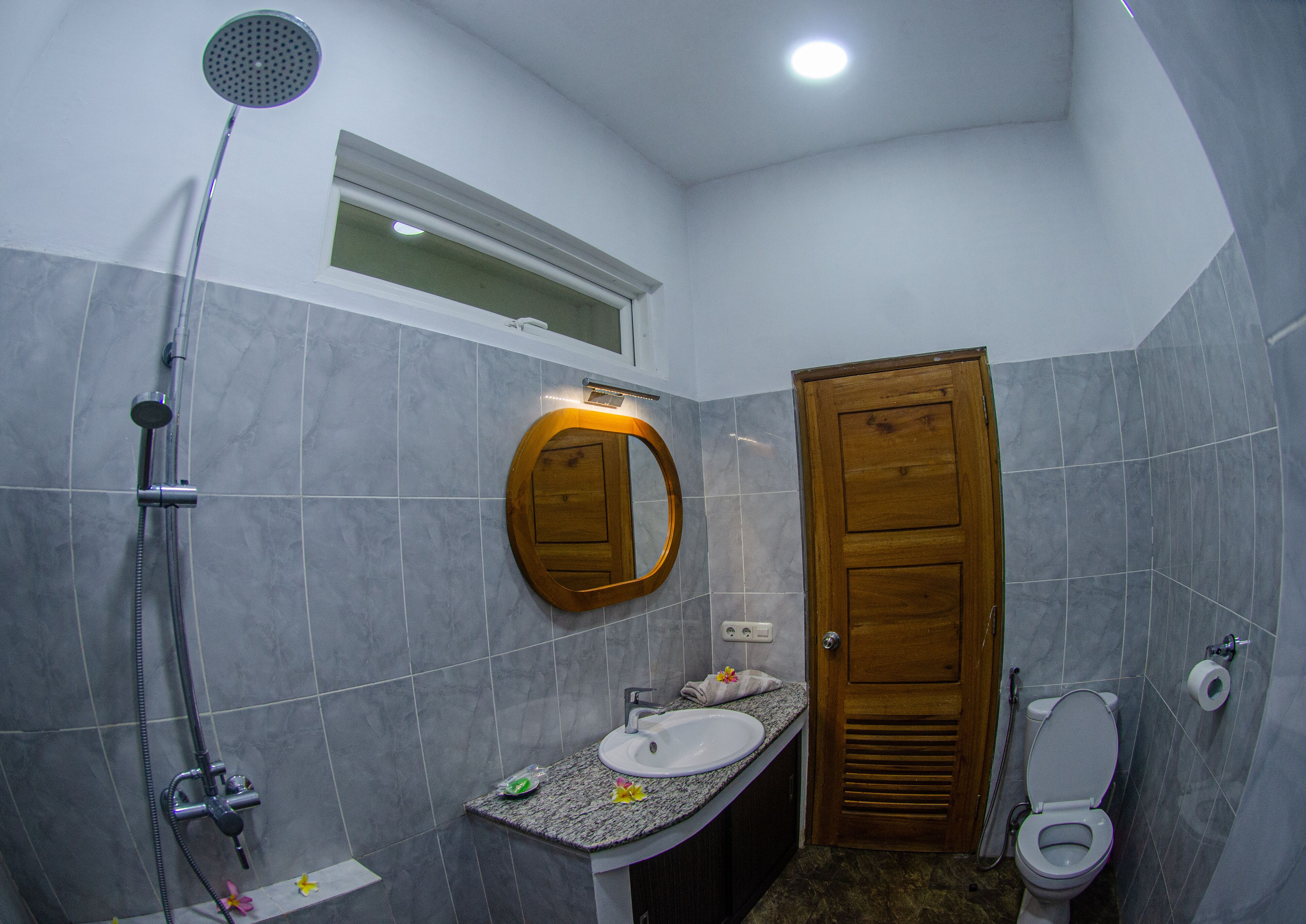 A bathroom with a shower, sink, toilet, and a wooden door.