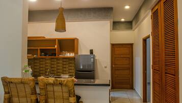 A kitchen with a refrigerator, wooden cabinets, and a dining area with chairs.