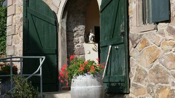A stone building with a statue in the doorway, green shutters, and a potted plant.