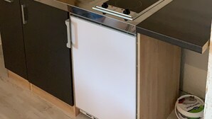 Una cocina compacta con un lavamanos, un refrigerador pequeño y armarios oscuros.