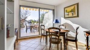 Zona pranzo con tavolo e sedie, una lampada e vista su un patio esterno attraverso ampie finestre.