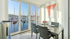 Een eetruimte met uitzicht op een jachthaven, een gedekte tafel voor twee personen en een modern abstract schilderij aan de muur.