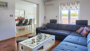 Una sala de estar moderna con un sofá gris, una mesa de centro de vidrio y un área de comedor visible a través de un puerta abierta.