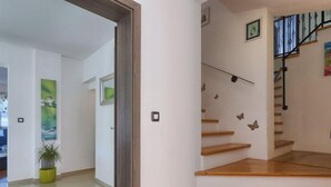 Un interior moderno con una escalera, escalones de madera, una planta en maceta y vistas de una habitación con un cuadro abstracto verde.
