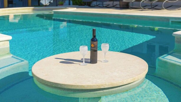Zona de piscina con sillones de descanso y una mesa con una botella y vasos.