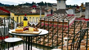 Una terraza en la azotea con una mesa dispuesta para una comida, que incluye queso, frutos secos y copas de vino.