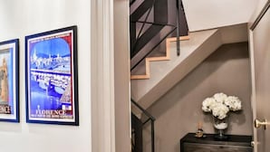Un pasillo con carteles de viajes enmarcados, una escalera de diseño moderno y una pequeña mesa con un florero.